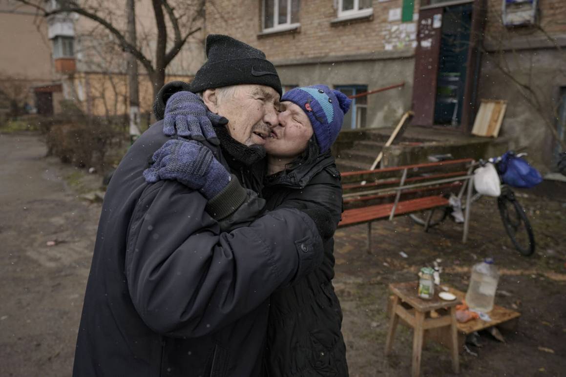 En kvinne kysser en mann mens hun lager mat på åpen ild utenfor en bygård uten strøm, vann eller gass i Bucha, Ukraina. Foto: AP Photo/Vadim Ghirda.